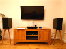 Load image into Gallery viewer, Wooden TV stand with a television, KEF R3 speakers on Cherry speaker stands by Audio Chic, and electronic devices in a room.
