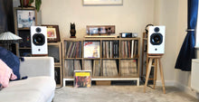 Load image into Gallery viewer, Living room with ATC scm19 speakers, on Ash Heron speaker stands by audio chic and a record player, and vinyl records on a shelf.