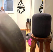 Load image into Gallery viewer, Black HomePod speaker on a wooden speaker stand by audio chic in a room with exercise equipment.