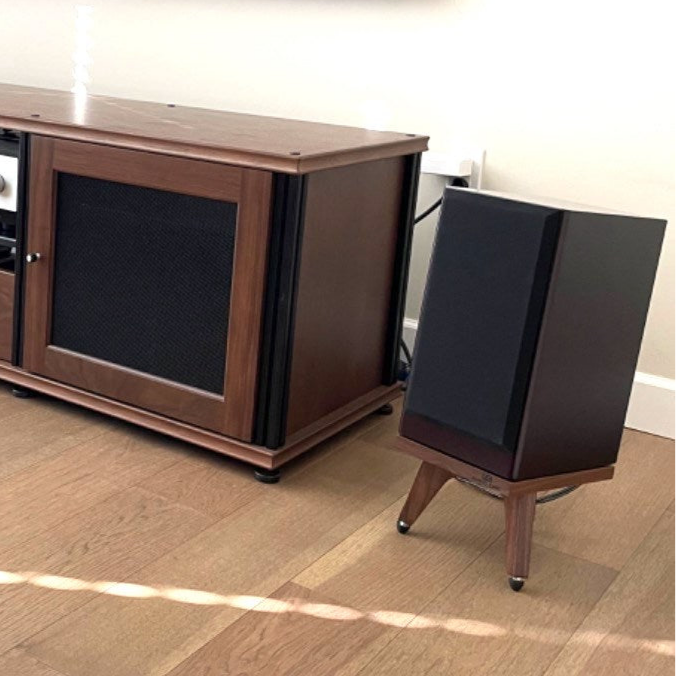 Wooden entertainment console with a black ascent acoustic sierra lx drunken snipe speaker stand on a wooden floor.