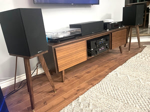 Wooden entertainment console with speakers on a pair of speaker stands in walnut by audio chic in a room setting