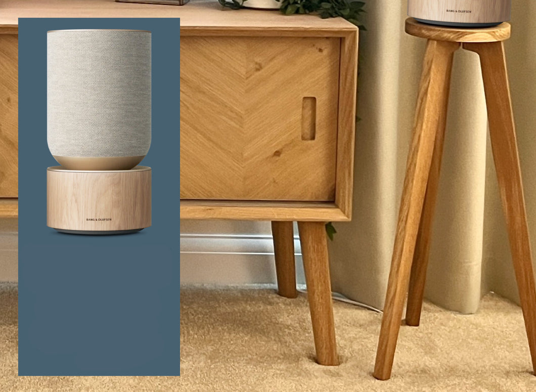 Single circular speaker stand made of wood with a speaker on top, placed on a floor beside a piece of furniture.