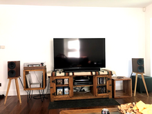 Load image into Gallery viewer, Living room with a TV on an entertainment console, Buchardt-S400-speakers-on-Bittern-speaker-stands-by-audio-chic, and decorative items.