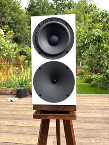 Speaker on a stand outdoors with greenery in the background