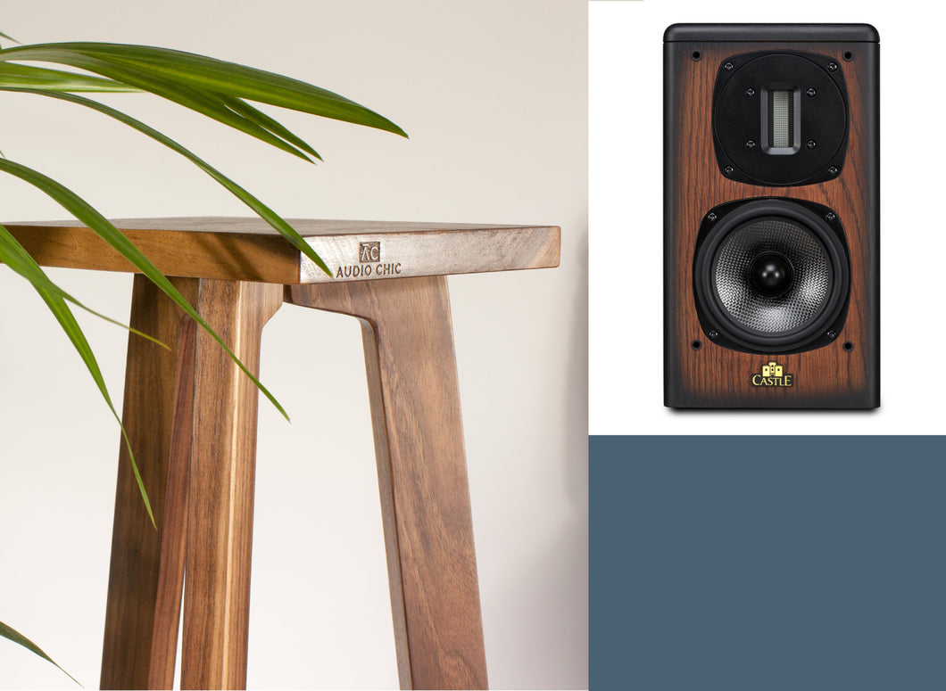 A pair of Castle Acoustics Richmond IV speaker stands in walnut finish, with a textured isolation plinth, shown in an elevated position with a set of Avon 1 speakers on top, placed against a backdrop featuring a green potted plant and a textured white wall.