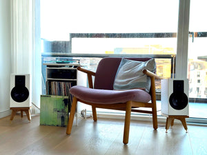 Modern armchair with speakers and audio chic Drunken Snipe speeaker stands, books in a room with large windows