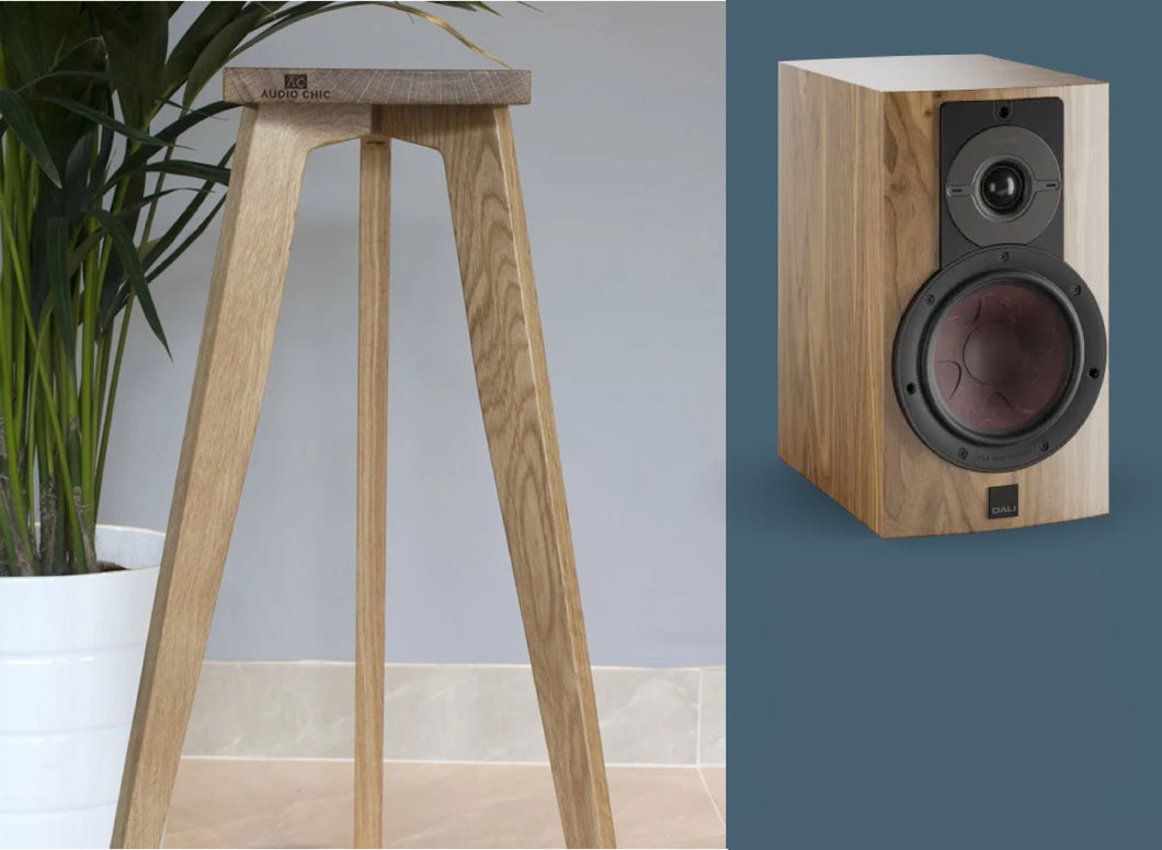 A Dali Rubikore 2 shaped speaker with a speaker stand in oak finish, featuring a three-legged design and a shaped top plate.