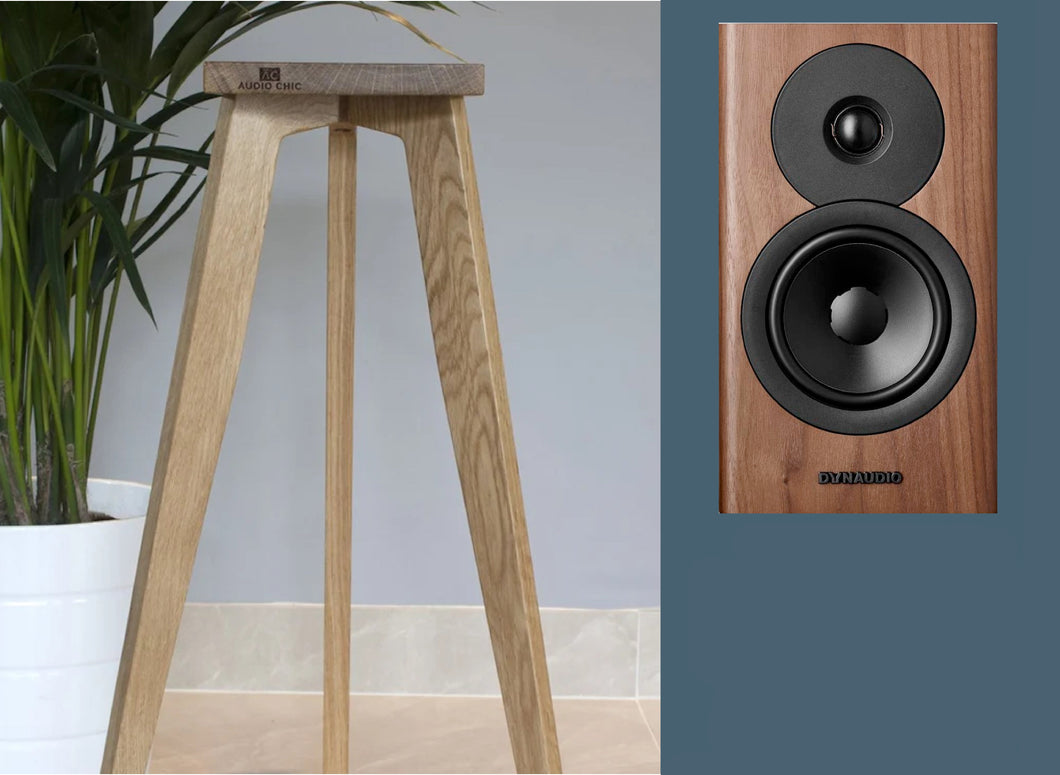 A pair of Dynaudio Avoke 10 speaker stands in oak finish, shown with a plant and a wooden floor in the background, indicating the product's placement and sound quality enhancement for speakers.