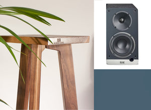 An image showing a Elac Debut ConneX DCB41 powered speaker with a tripod speaker stand. The stand has a wooden top, with the brand logo visible on the front of the speakers.