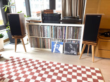 Load image into Gallery viewer, Record player with vinyl records on a shelf in a room with Harbeth C7ES3 speakers on Egret speaker stands with isolation plinths with a checkered rug.