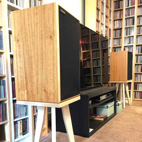 Harbeth-M30.2-XD-500-egret-speaker-stand-in-maple-by-audio-chic in a room with wall to wall bookshelves.