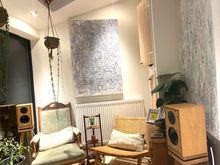 Load image into Gallery viewer, Living room with wooden Harbeth-P3ESR speakers, on a Heron-700-oak-speaker-stands-with-plinths-by-audio-chic armchair, and an abstract painting on the wall.