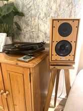 Load image into Gallery viewer, Harbeth-P3ESR-Speaker-Oak-Heron-speaker-stand-by-audio-chic. Wooden speakers on a stand next to a record player on a wooden cabinet with a marble wall in the background.