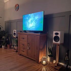 Harmony Speaker stands by Audio chic in a Living room setup with a TV, speakers, and decorative items.