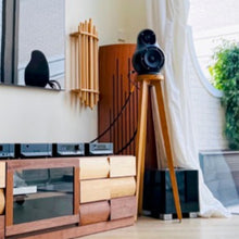 Load image into Gallery viewer, JERN-15-crane-speaker-stands-in-oak-by-audio-chic in a Modern living room with a wooden entertainment console and large TV.