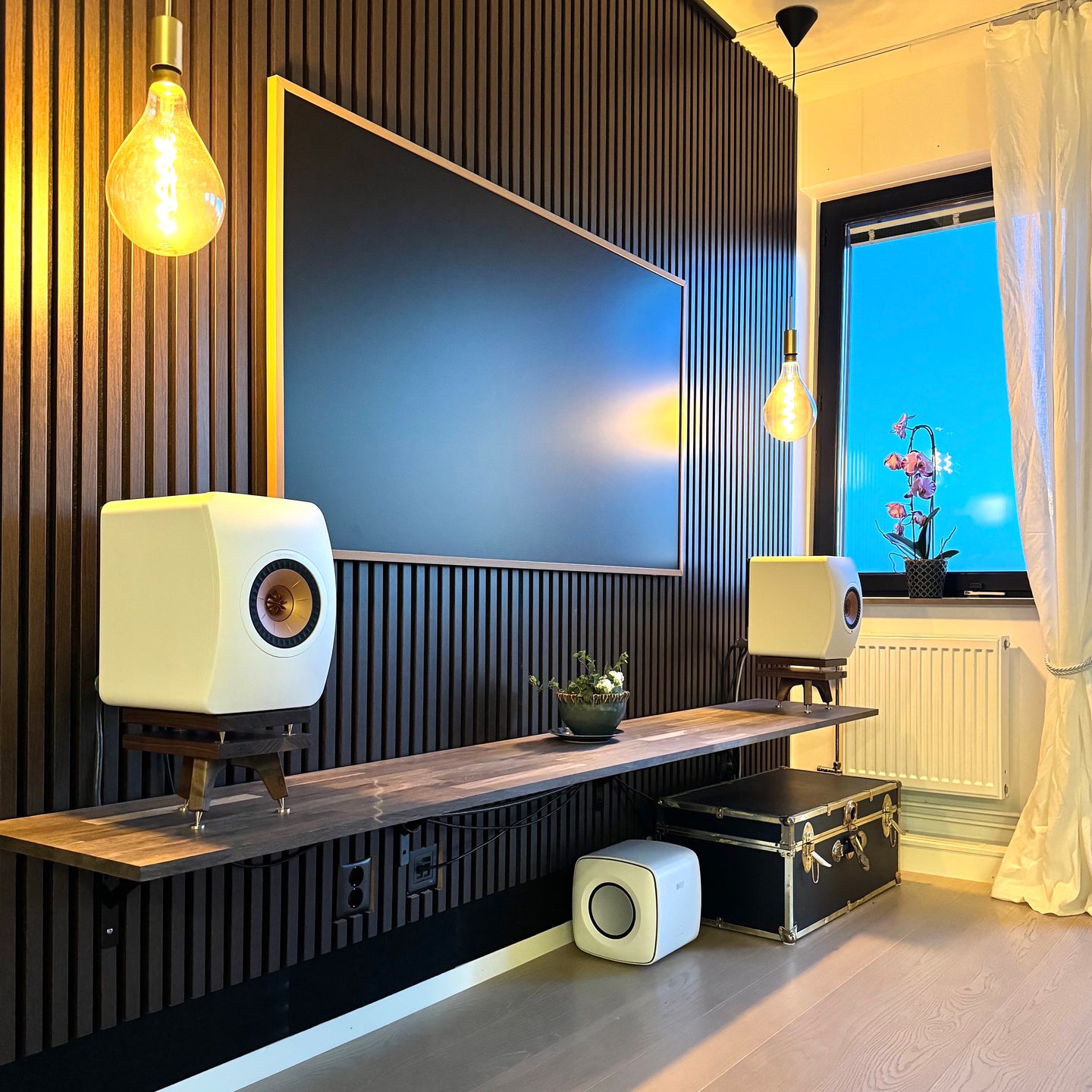 Modern living room with a large TV, KEF-LS50-Metas-snipe-speaker-stands-in-Walnut-with-Plinths-by-audio-chic, and decorative elements.