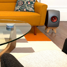 Load image into Gallery viewer, Modern living room with orange sofa, glass coffee table, and JEF LS50W on a short kite speaker stand.