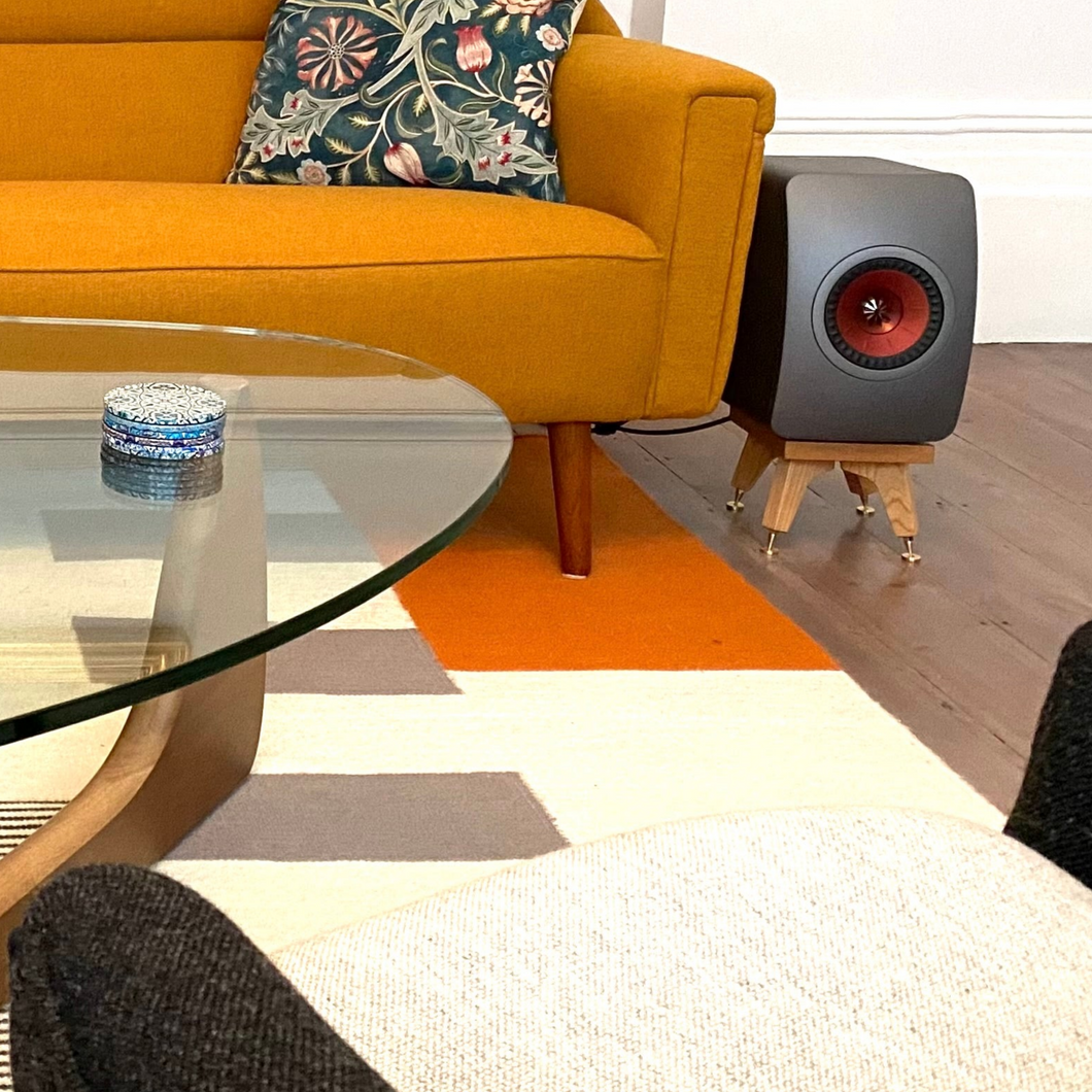 Modern living room with orange sofa, glass coffee table, and JEF LS50W on a short kite speaker stand.