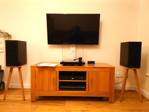 Wooden TV stand with a television, KEF R3 speakers on Cherry speaker stands by Audio Chic, and electronic devices in a room.