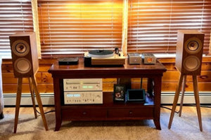 Living room with a wooden entertainment console, KEF R3 speakers on Walnut speaker stands, and blinds.