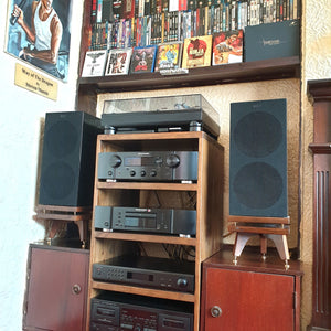 Audio equipment, including KEF R3 speakers with grille on Walnut snipe speaker stands from Audio Chic and amplifiers on a wooden cabinet.