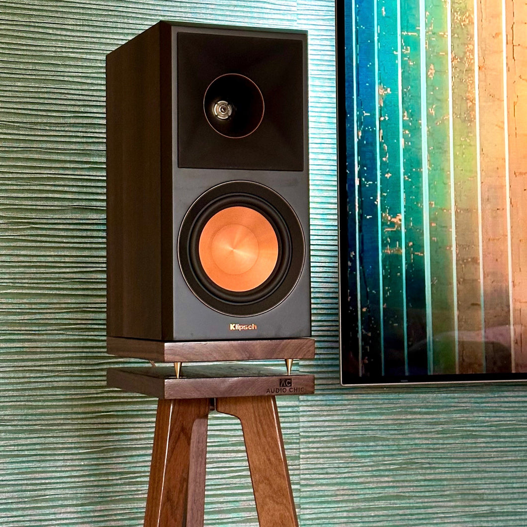 Klipsch-RP500M-II-Walnut-700-speaker-stand-by-audio-chic against a textured wall with a colourful abstract painting.