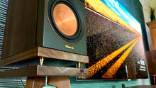 Load image into Gallery viewer, Close-up of a Klipsch RP500MII speaker on an Audio Chic speaker stand, showing the Audio Chic logo brand with a scenic display in the background