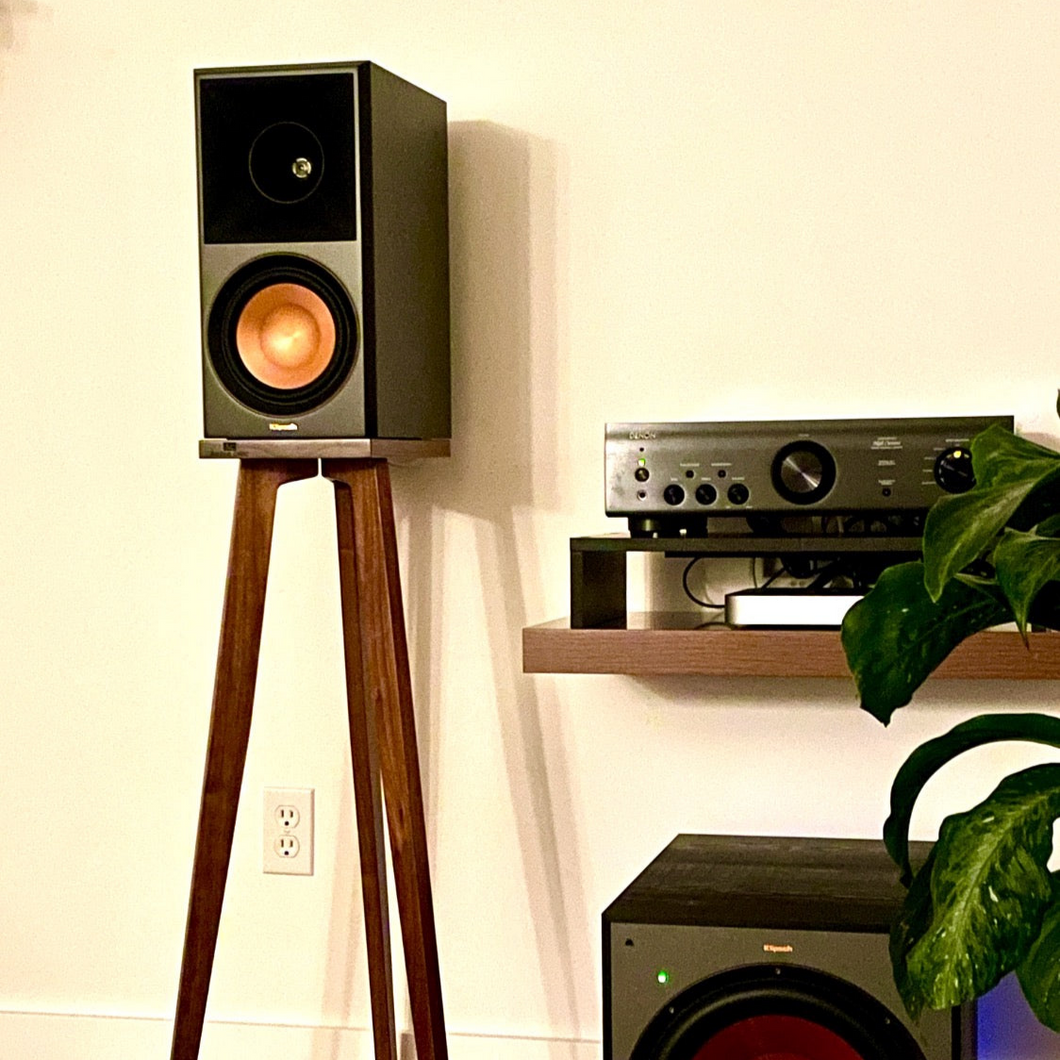 Klipsch-Reference-Premiere-II-c-100-Watt-900-crane-Speaker-stand-by-audio-chic next to a shelf with audio equipment and a plant.