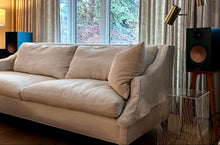 Load image into Gallery viewer, Beige sofa in a living room with curtains and Monitor Audio Siver 100 speakers on audio chic speaker stands in walnut.