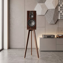Load image into Gallery viewer, A tall wooden floor-standing Audio Chic speaker stand on a tree legs with the Monitor Audio Silver 100 8G speaker, shown in a modern living room setting with a console, record player, and geometric wall decor.