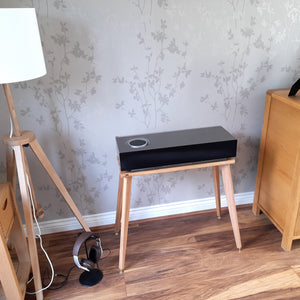 Naim-Audio-mu-so-2nd-centre-speaker-stand-by-audio-chic with Wooden side table, lamp, and wooden cabinet in a room.