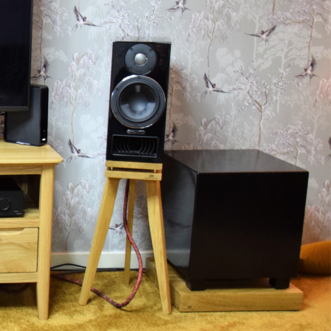PMC-twenty5.22i-bittern-550-oak-speaker-stands-by-audio-chic against a patterned wall.