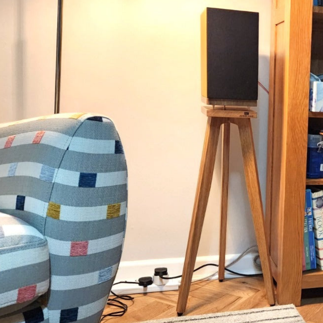 Pro-ject-speaker-box-5-S2-The-Heron-700-Oak-with-Plinths-from-audio-chic next to a colourful chair in a room.