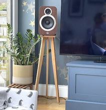 Load image into Gallery viewer, q-acoustics-3020i-snipe-speaker-stand-in-oak-by-audio-chic in a living room setting with a television and plant.
