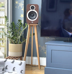 q-acoustics-3020i-snipe-speaker-stand-in-oak-by-audio-chic in a living room setting with a television and plant.
