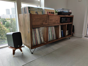 Q-acoustics-3010i-snipe-speaker-stands-in-walnut-by-audio-chic with Wooden record player console with vinyl records in a room with large windows.