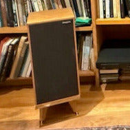 Rogers-hifi-LS7t-speakers-on-Drunken-Snipe-speaker-snipes-by-audio-chic in a home library setting, with the speakers positioned on the stands and surrounded by books on shelves.