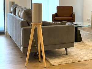 Modern living room with gray sofa, brown armchair, and wooden side table and a Sony hT-A9 speaker on a wooden speaker stand by audio chic