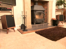 Load image into Gallery viewer, Wharfedale-Denton-85-drunken-snipe-in-walnut. In a room setting with a stove fire and rug. Speaker-stands-by-audio-chic