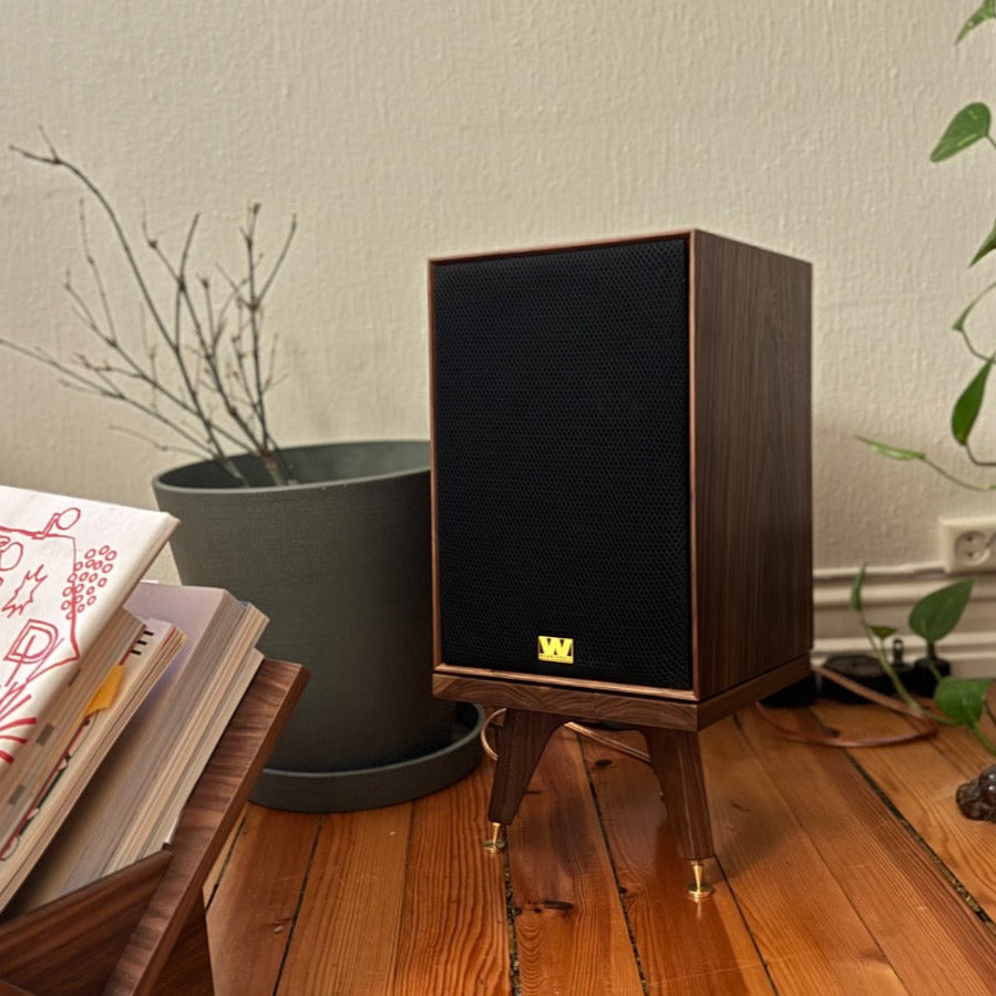 Wharfedale-Super-Denton-Drunken-Snipe-speaker-stand-by-audio-chic. Wooden speaker on a wooden floor with books and a plant in the background