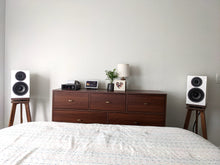 Load image into Gallery viewer, Wooden dresser with Wharfedale-diamond-12.2-speaker-stands-in-walnut-by-audio-chic- on either side against a plain wall.