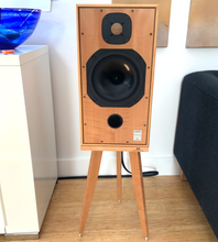 Load image into Gallery viewer, Wooden Harbeth C7ES3 speaker on a speaker stand by Audio Chic in a room with a white wall and a blue object in the corner.