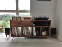 Load image into Gallery viewer, Q-acoustics-3010i-snipe-speaker-stands-in-walnut-by-audio-chic with a Wooden record player console with vinyl records and speakers in a room with large windows.