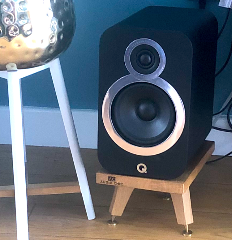 q-acoustics-3020i-snipe-speaker-stand-in-oak-by-audio-chic against a blue wall