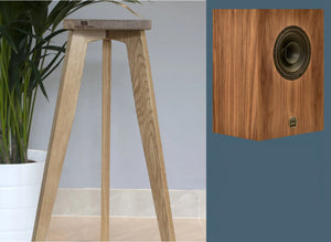 An elegant three-legged monitor speaker stand made of oak, with a compact alnico monitor speaker resting on top. The stand is presented in a home setting, indicating its use for supporting and displaying speakers.
