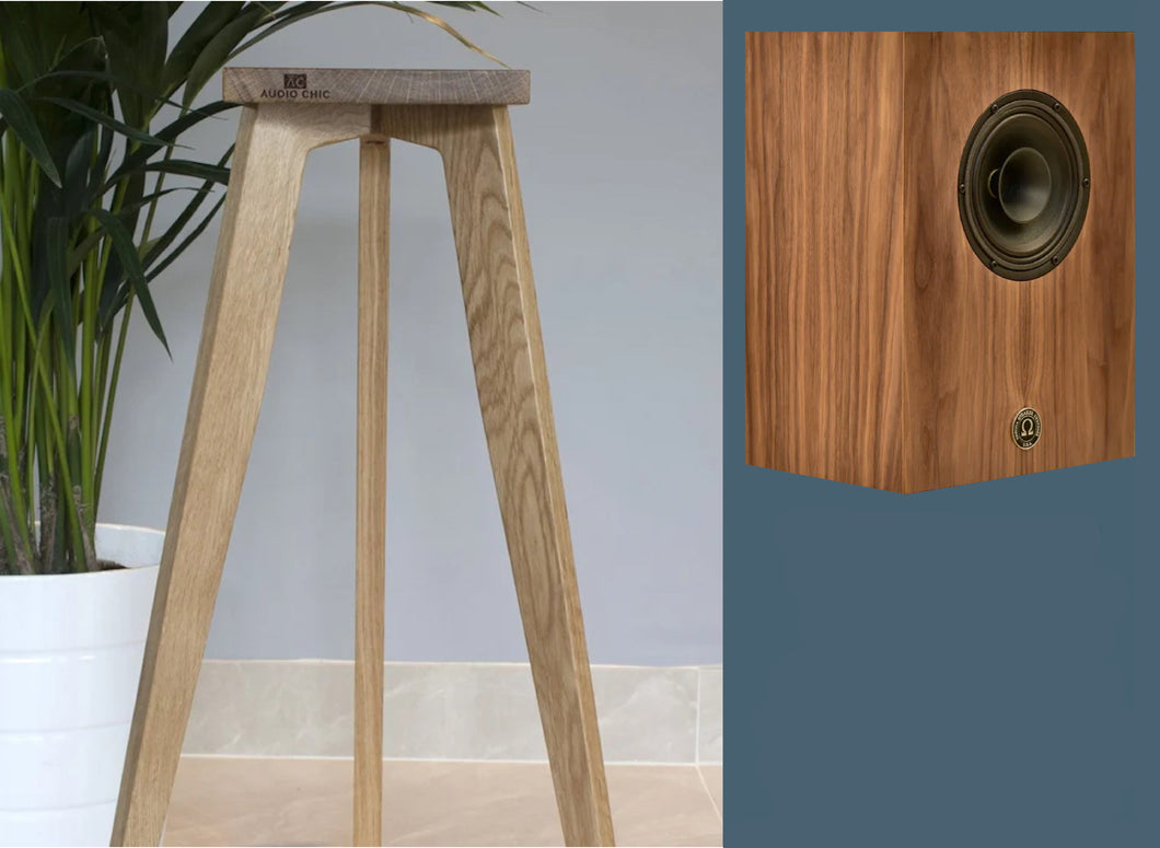 An elegant three-legged monitor speaker stand made of oak, with a compact alnico monitor speaker resting on top. The stand is presented in a home setting, indicating its use for supporting and displaying speakers.